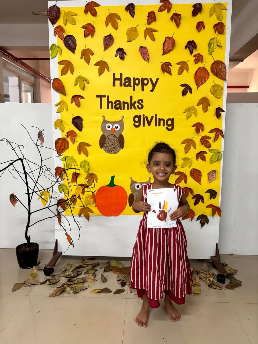Little girl proudly holding her painted handprint turkey artwork in front of Thanksgiving board